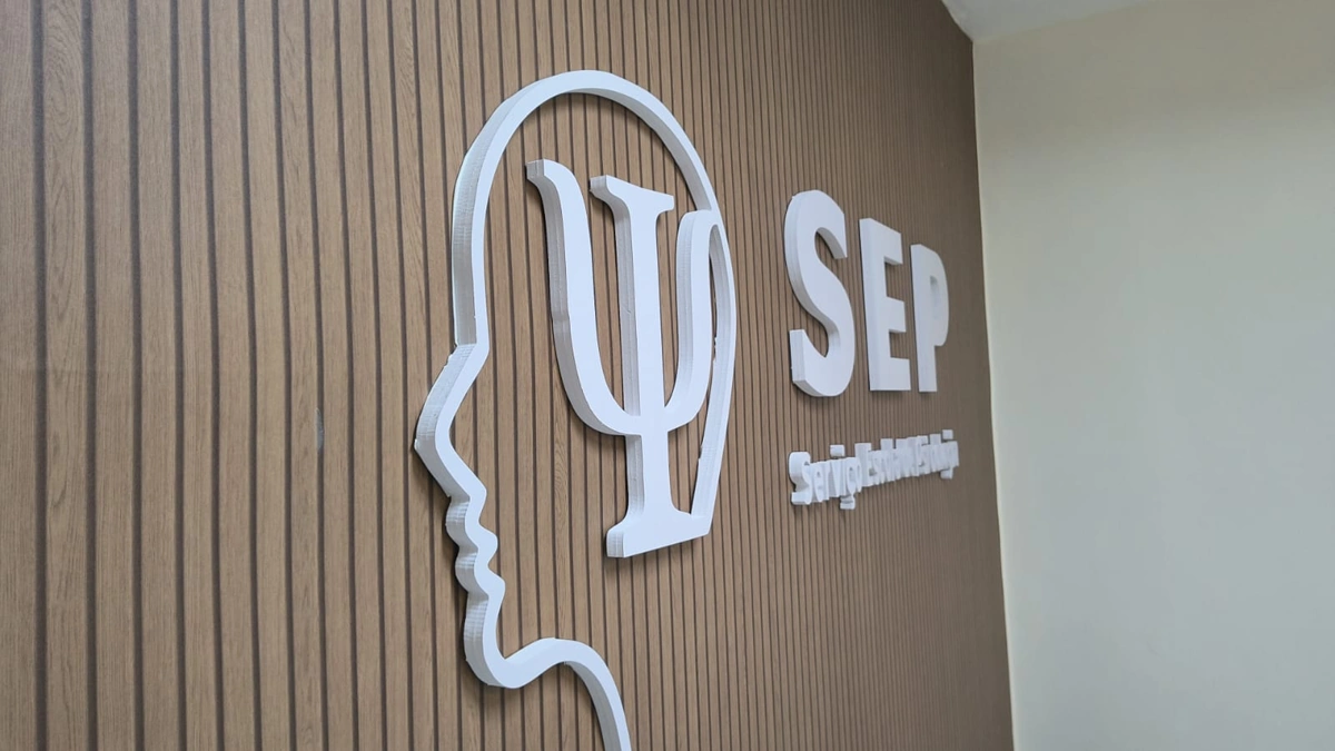 Letras e símbolo em relevo aplicados sobre painel ripado.